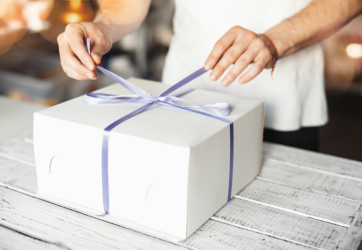 Young cook ties violet ribbon on white cake packaging